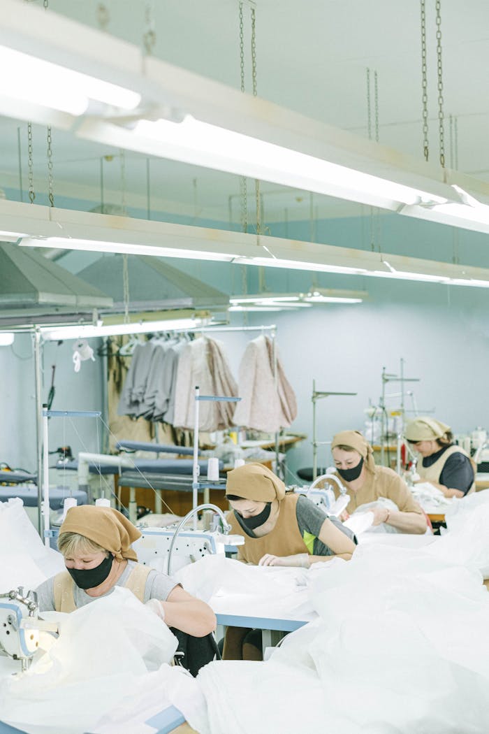 Women sewing with machines in a textile factory, wearing face masks and headscarves.
