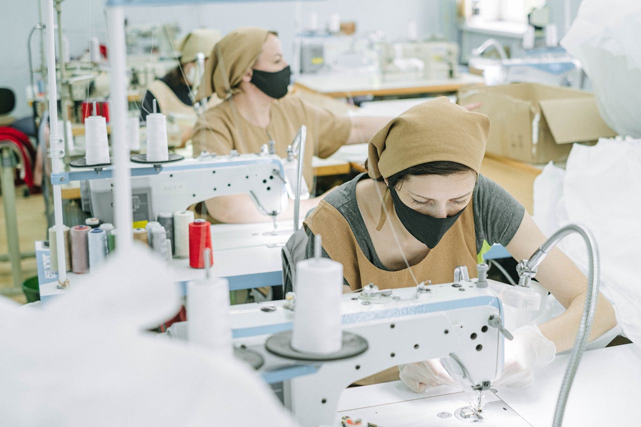Women in a textile factory, wearing face masks, skillfully using sewing machines.